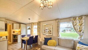 Ein gemütliches Zimmer mit Essbereich, einer Couch mit Kissen, einem Fenster mit Vorhängen und einer Chandelüster.