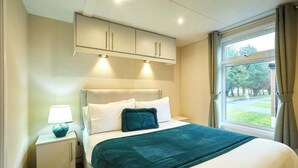 Hotelkamer met een bed, nachtkastje, raam met uitzicht op bomen en inbouwmeubels boven het bed.