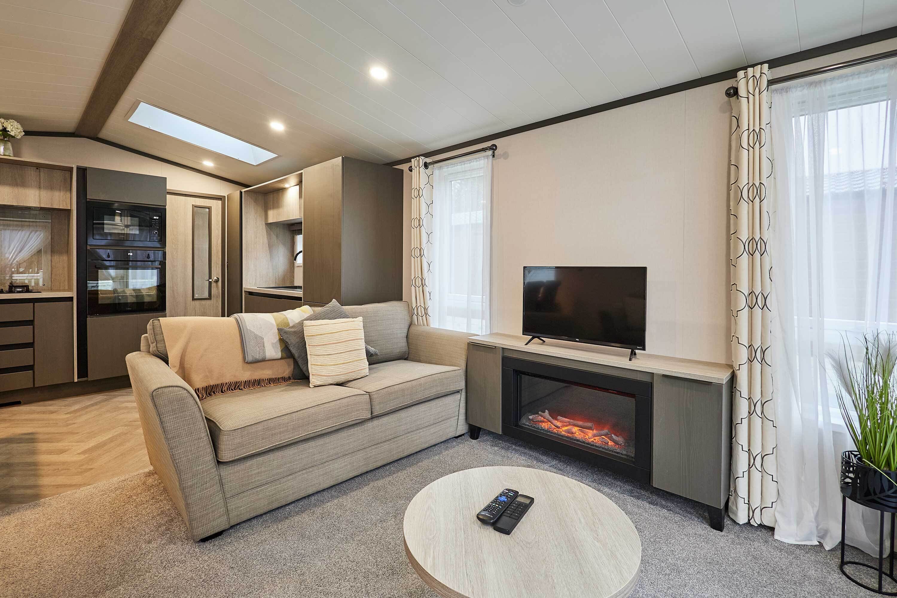 A modern living room with a sofa, a fireplace, a TV, and a kitchen area with cabinets and a refrigerator.