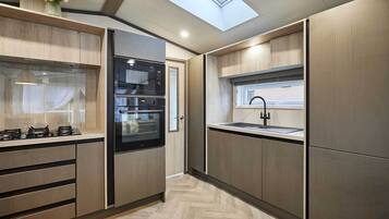 A modern kitchen with built-in appliances, a skylight, and a view of the adjacent room.