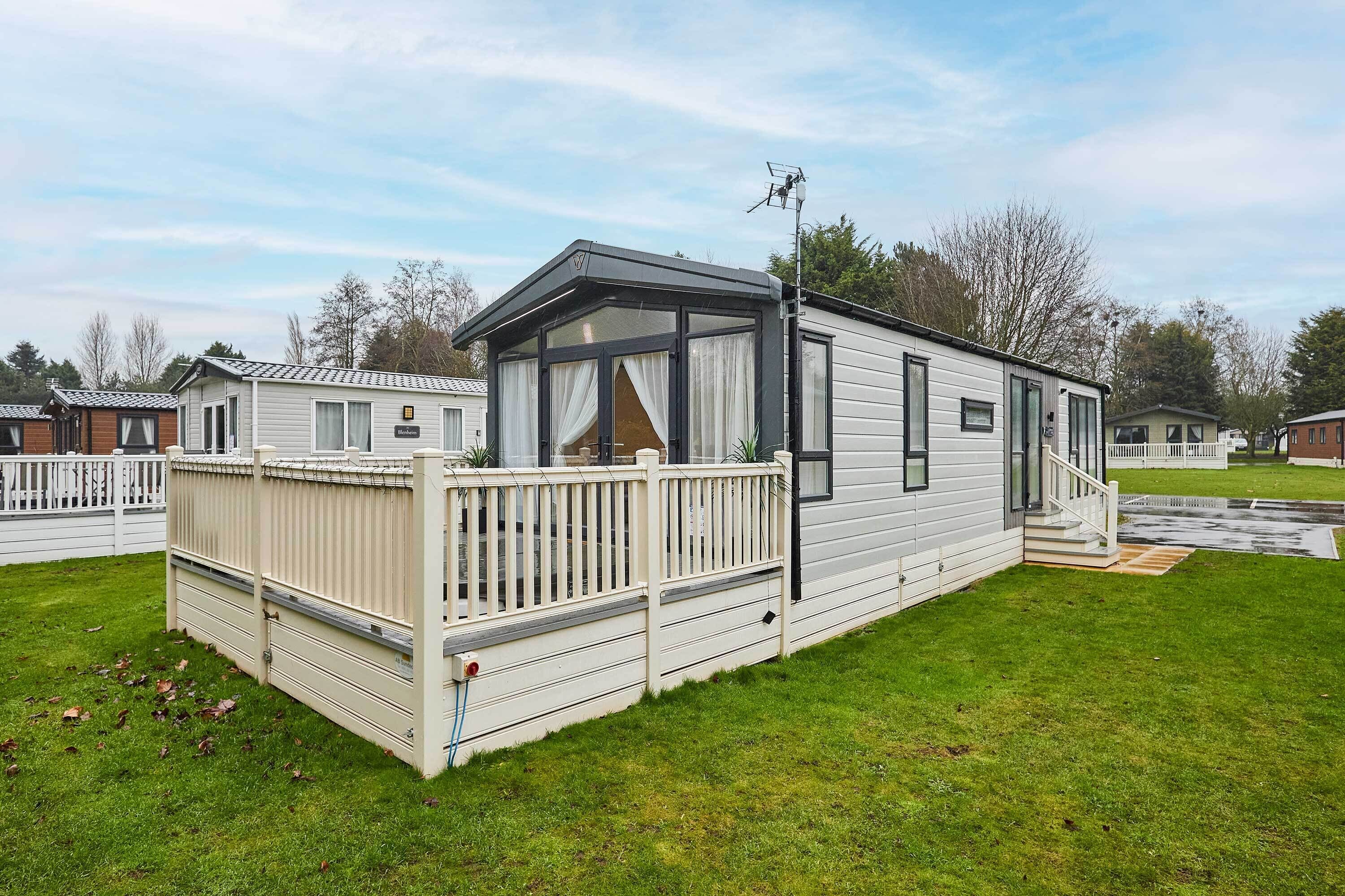 A single-story mobile home with a fenced deck, large windows, and a covered porch.