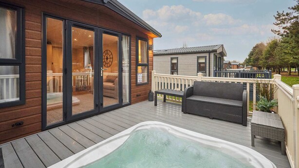 Eine Holzterrasse mit Whirlpool, Korbmöbeln und Blick auf ein Haus mit großen Fenstern.