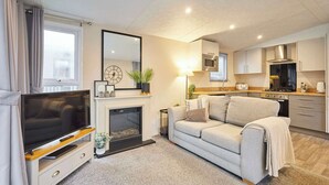 Ein gemütlicher Wohnbereich mit Fernseher, Kamin, Sofa und Küchenzeile, sowie einem großen Spiegel.