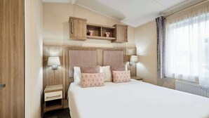 A hotel room with a large bed, wooden headboard, two bedside tables with lamps, and a window with curtains. - Host & Stay | Lakeshore Lodge (Pocklington)