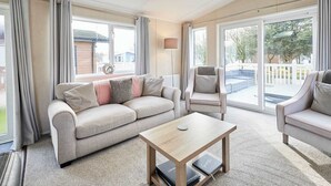 A spacious living room with a beige sofa, two armchairs, a wooden coffee table, and a large sliding glass door leading to an outdoor area. - Host & Stay | Lakeshore Lodge (Pocklington)