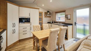 Een moderne keuken met witte kastjes, een houten eettafel en beigekleurde stoelen.
