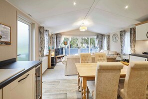 A spacious living area with a dining table, comfortable seating, a television, and a view of the outdoors. - Host & Stay | Country Cabin Lodge (Pocklington)