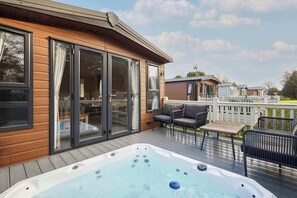 Une terrasse en bois avec un jacuzzi, des sièges d’extérieur et une vue sur les maisons voisines.