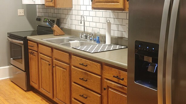 Una cocina con armarios de madera, un refrigerador de acero inoxidable, un microondas y un lavamanos.