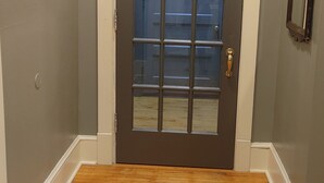 Una habitación con una puerta de madera oscura, un zócalo blanco y piso de madera.
