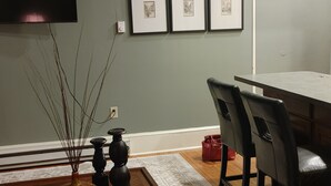 Una sala de estar con una mesa de centro de madera, un sofá rojo, una mesa de comedor con sillas, un ventilador de techo y cuadros en la pared.