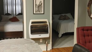 Una habitación con cama, calefactor, una silla y un cuadro en la pared.