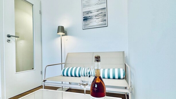 Et værelse med en seng, et sengebord med en flaske og et glas, en lampe og et billede i ramme på væggen.