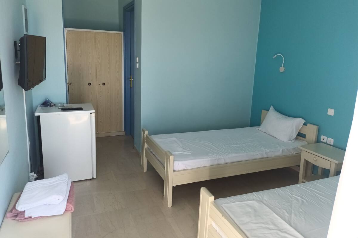 A bedroom with two single beds, a desk with a chair, a wardrobe, and a television on the wall.