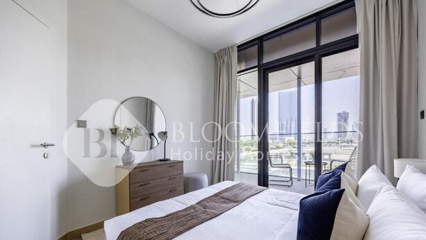 Una habitación de hotel moderna con una cama grande, un aparador, un espejo y vistas de la ciudad a través de amplias ventanas.