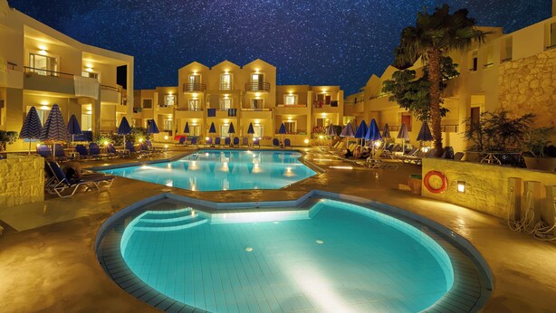 Une cour d’hôtel avec une piscine, des chaises longues et un ciel étoilé.