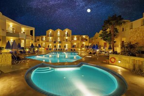 A hotel courtyard with a swimming pool, lounge chairs, and a starry night sky. - Bella Pais Hotel (Maleme)
