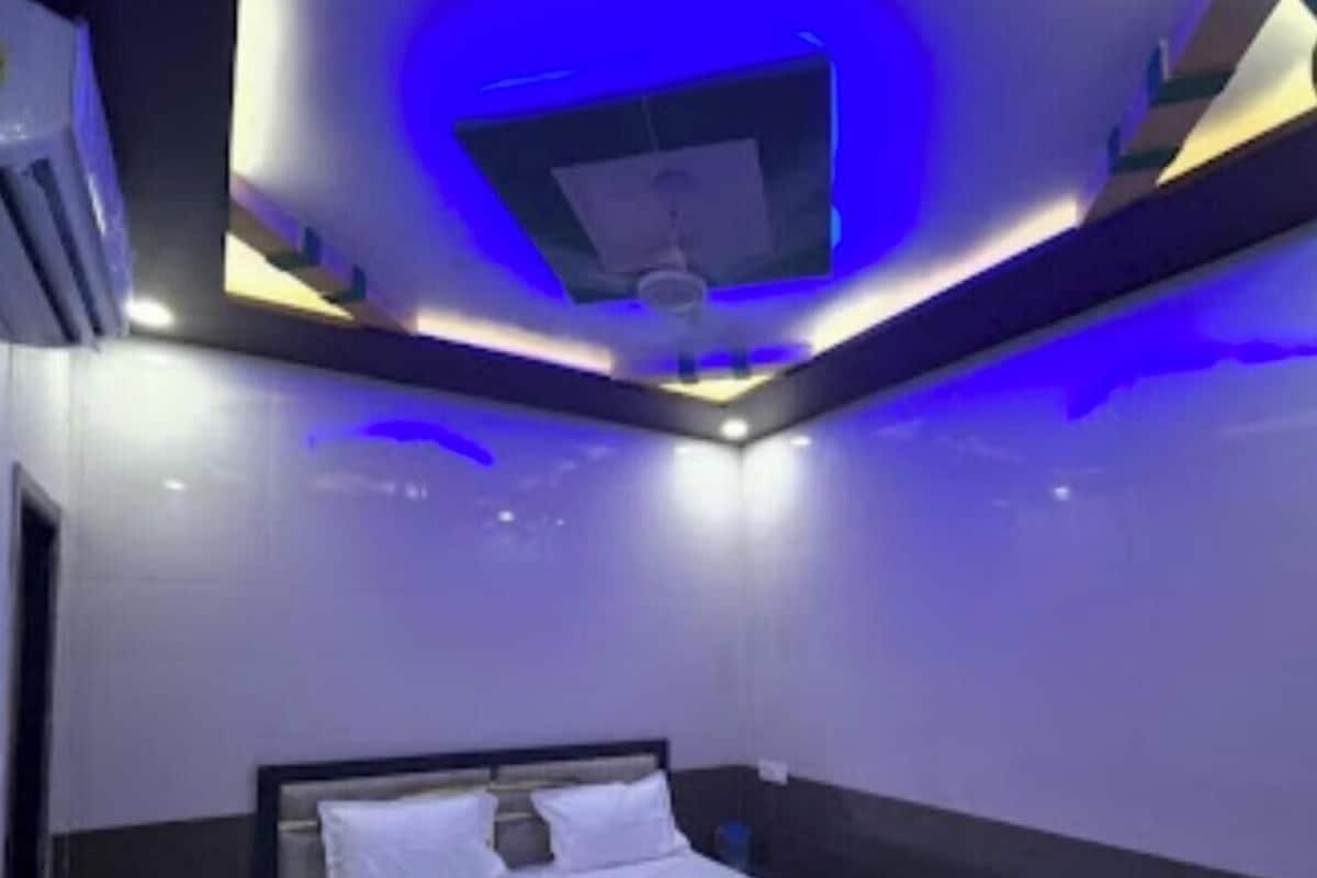 Un dormitorio moderno con cama, paredes oscuras e iluminación ambiental azul.