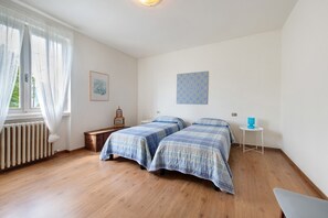 A bedroom with two beds, a radiator, a small table, and a picture on the wall.