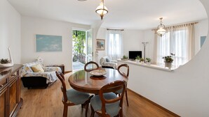 A dining area with a round wooden table, four chairs, a television, and a window with curtains. - Welcome to "Casa Al Lago" on Lake Iseo (Sulzano)