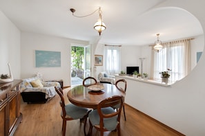 A dining area with a round wooden table, four chairs, a television, and a window with curtains.