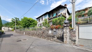 A two-story building with a stone wall, a garage, and a balcony with potted plants. - Welcome to "Casa Al Lago" on Lake Iseo (Sulzano)