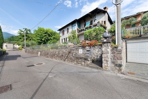 A two-story building with a stone wall, a garage, and a balcony with potted plants.