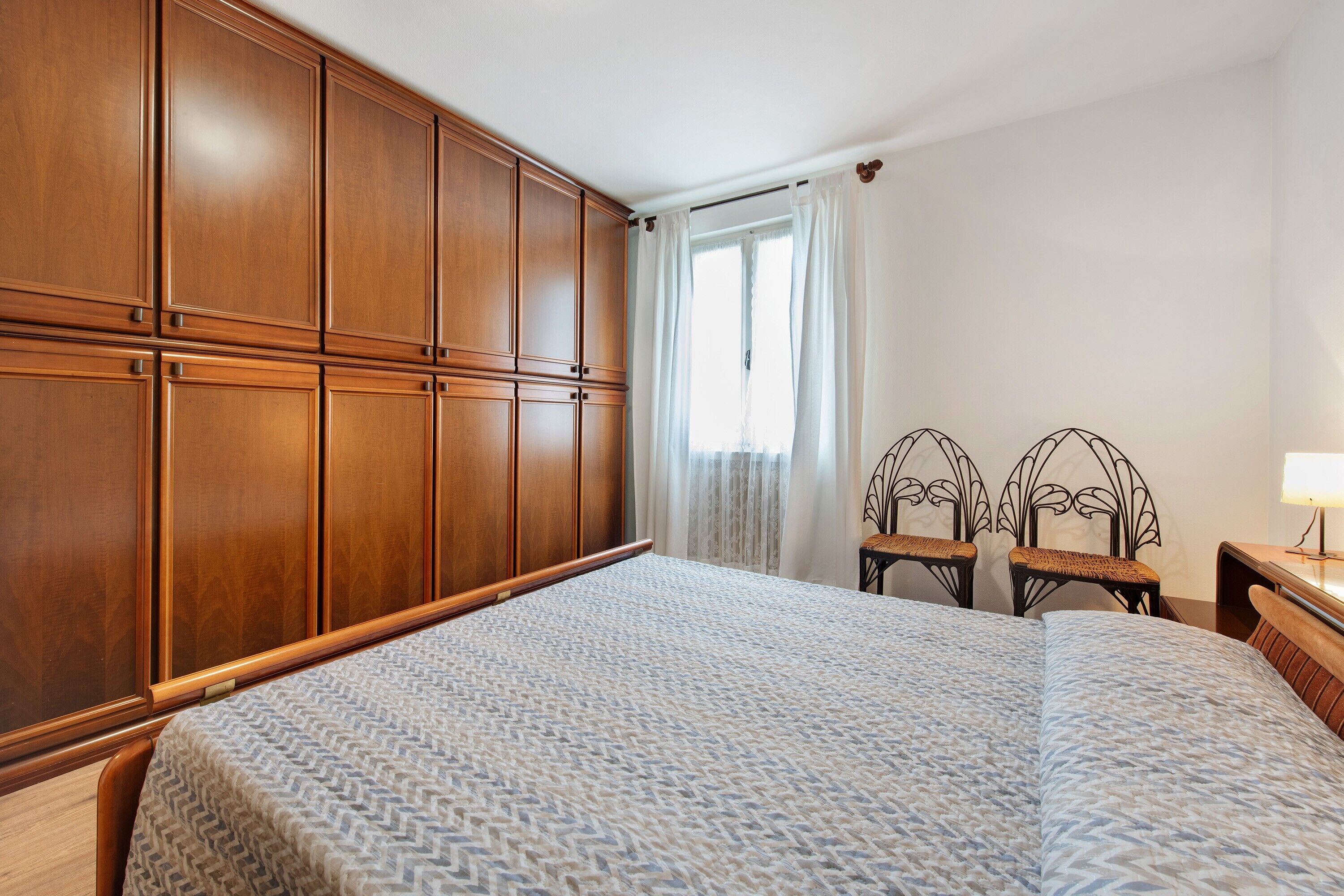 Ein Schlafzimmer mit einem großen Bett, einem Holzschrank, zwei Korbstühlen und einem Nachttisch mit Lampe.
