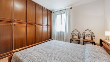 Ein Schlafzimmer mit einem großen Bett, einem Holzschrank, zwei Korbstühlen und einem Nachttisch mit Lampe.