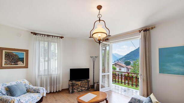A living room with a sofa, a wooden coffee table, a television, and a view of a balcony. - Welcome to "Casa Al Lago" on Lake Iseo (Sulzano)