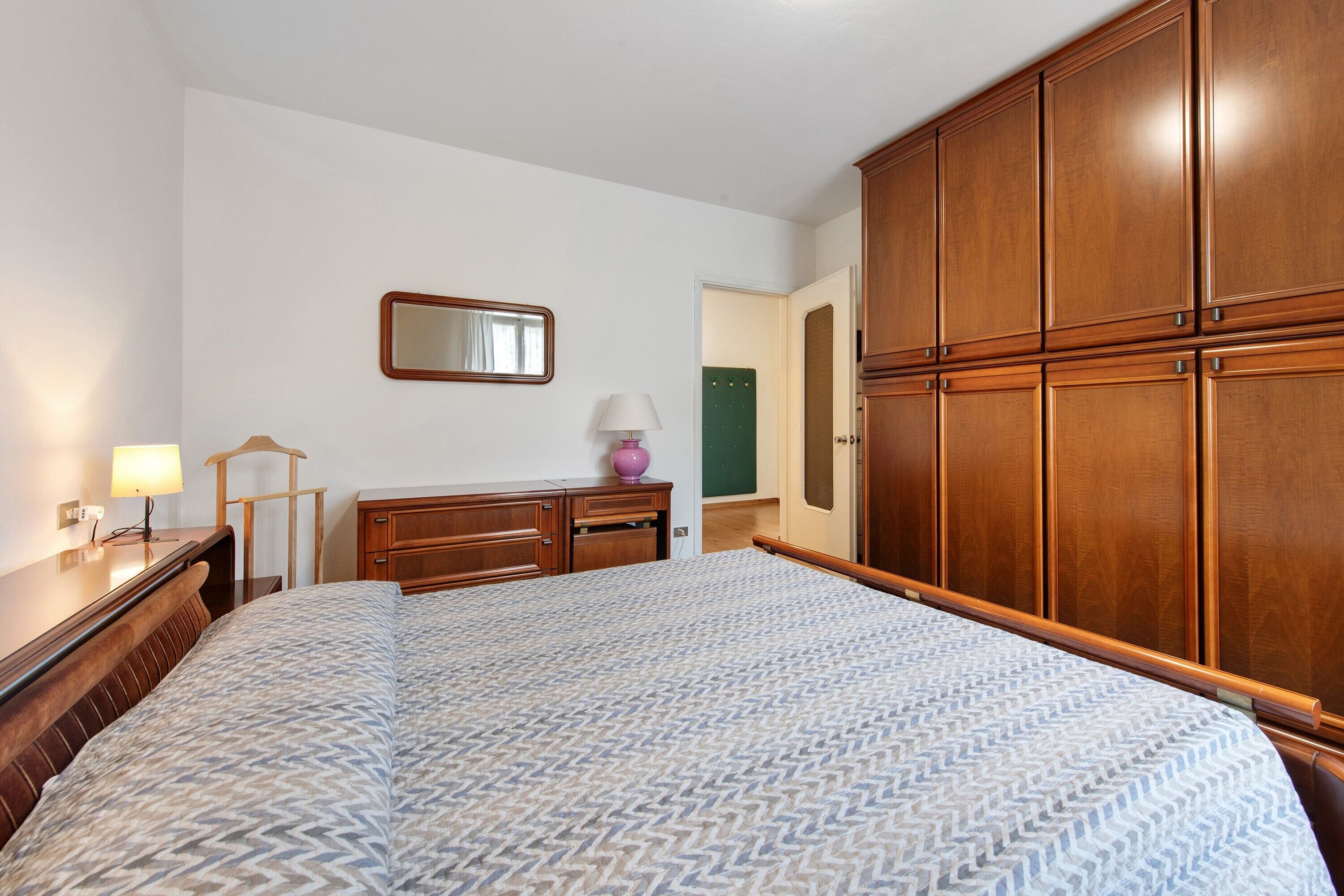 Une chambre à coucher comprenant un lit, une armoire en bois, un miroir, une lampe et une commode.