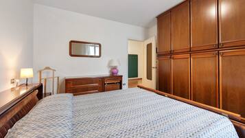 Une chambre à coucher comprenant un lit, une armoire en bois, un miroir, une lampe et une commode.