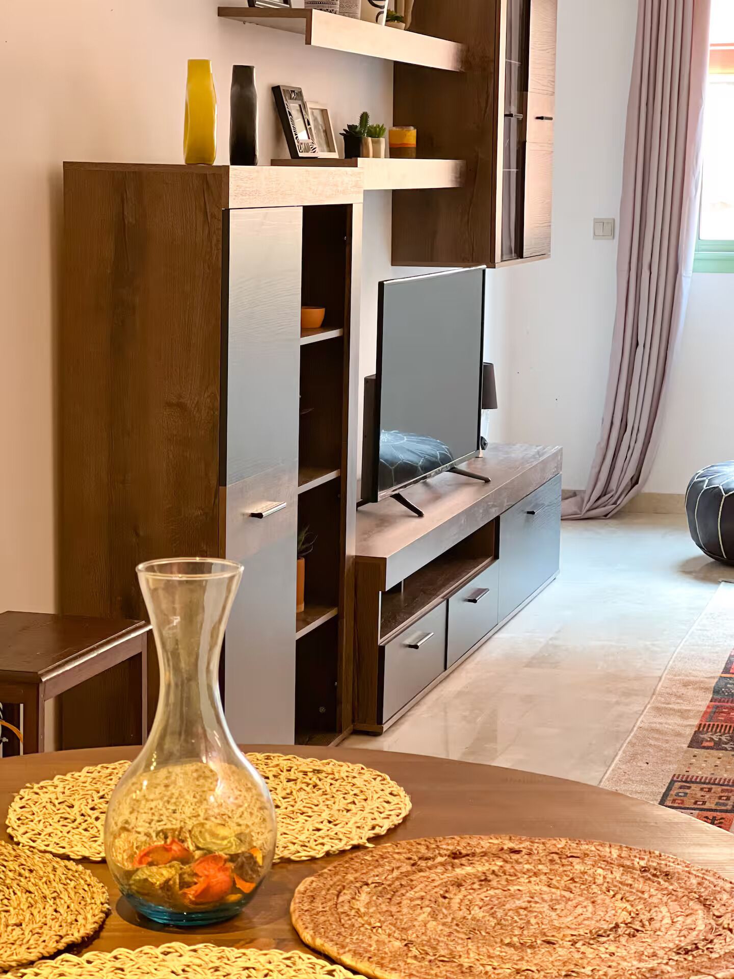 A modern living room with a TV, wooden furniture, and a decorative vase on a table.