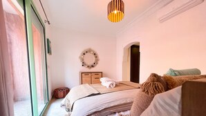 A bedroom with a bed, a bedside table, a mirror, a hanging light fixture, and a window. - 🌴  Chic & Modern Apartment in the Heart of Hivernage – Pool & Premium Comfort (Marrakech)