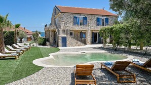 A stone building with a pool, lounge chairs, and a clear view of the sea. - Villa (Dobropoljana)
