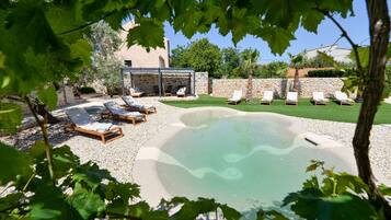 A pool area with lounge chairs, a stone wall, and a building in the background.