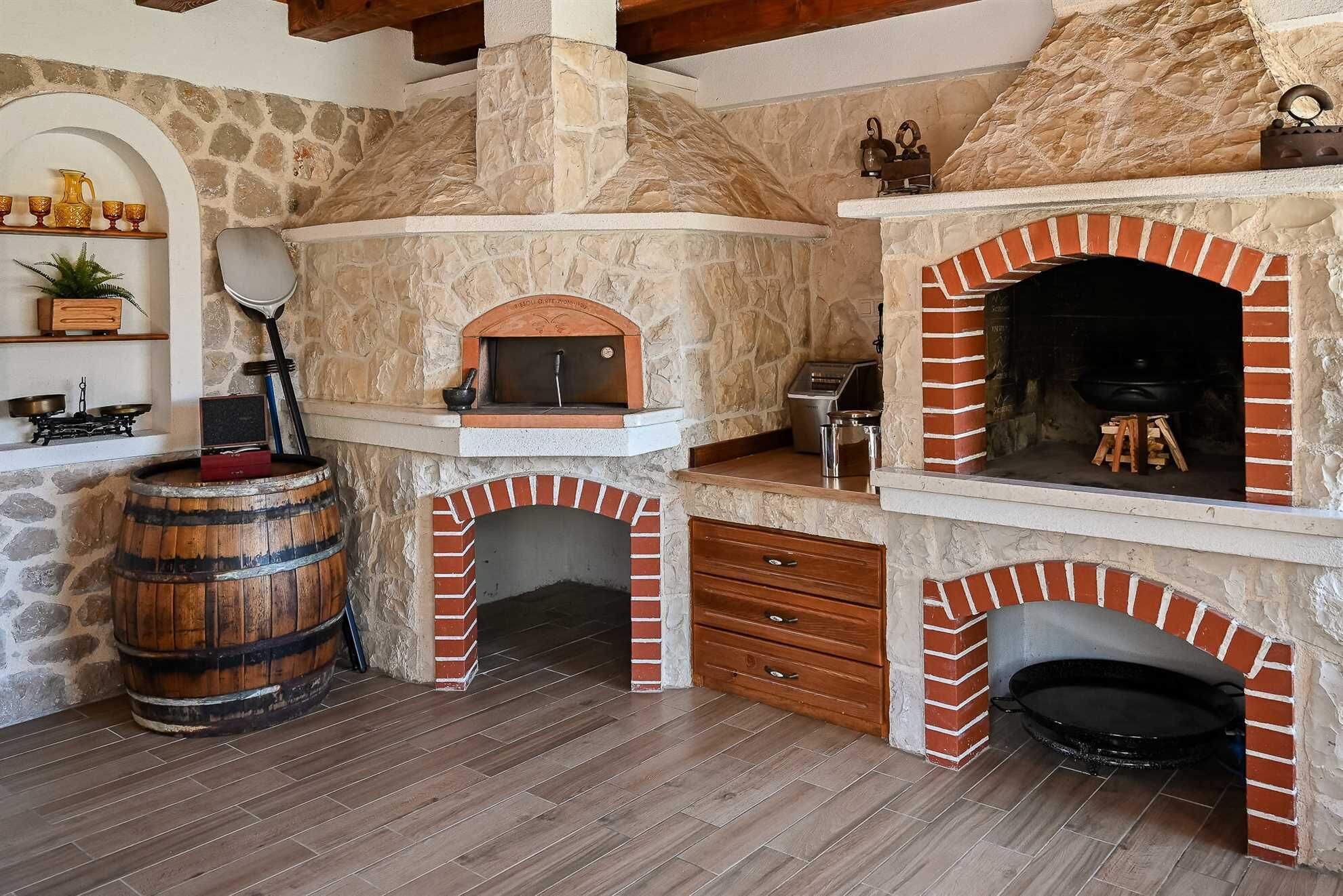 A stone-clad room with a wood-burning oven, a barrel, and a fireplace.