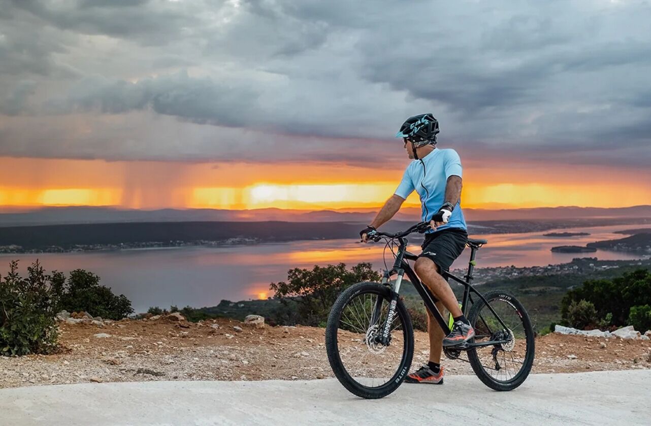 A person on a mountain bike overlooking a lake at sunset.
