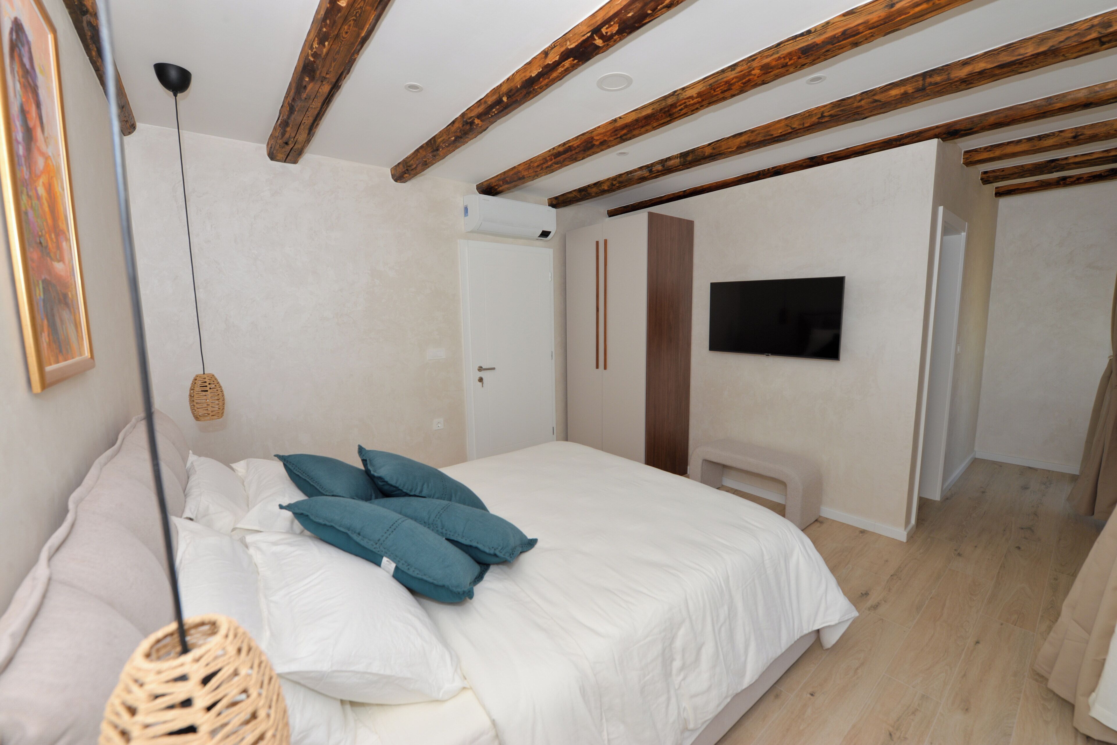 Une chambre à coucher avec un lit, des oreillers, une télévision, des poutres en bois et une porte.