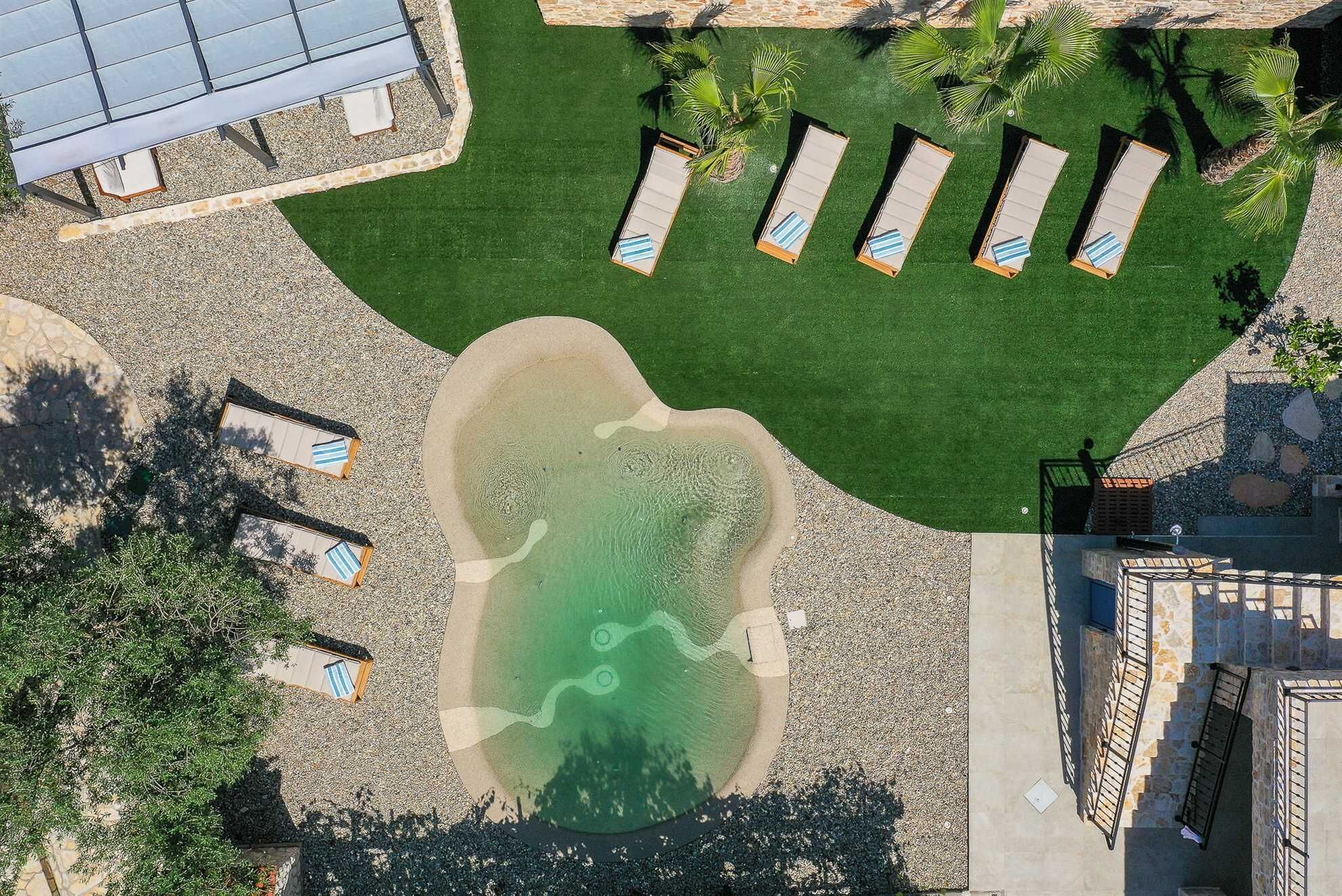 An aerial view of a resort with a swimming pool, sun loungers, and a covered area.