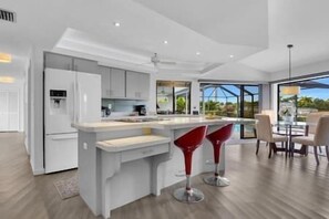 A modern kitchen with white cabinetry, a central island, and red bar stools. - Nautical Dream Gulf Access Home (Cape Coral)