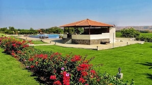 Un belvédère surmonté d’un toit en tuiles, une piscine et une pelouse bien entretenue agrémentée de plantes à fleurs.