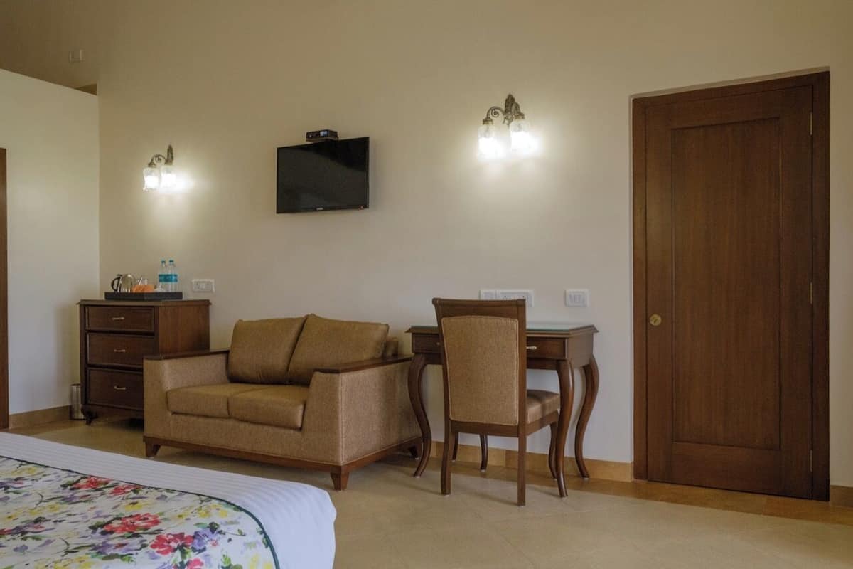 A hotel room with a bed, a sofa, a chair, a desk, a television, and a door.