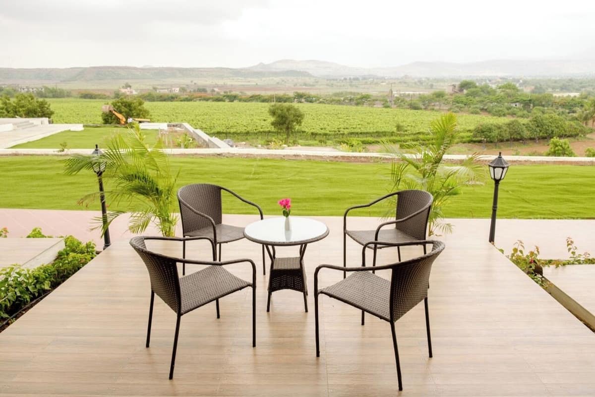 A patio with wicker chairs and a table, overlooking a vineyard.