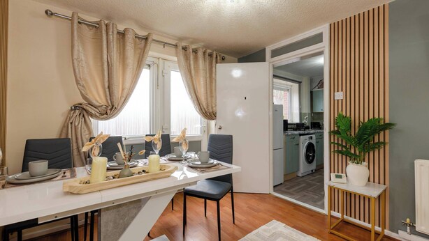 Una cocina moderna con lavadora, un comedor con mesa dispuesta para dos personas y una planta en maceta.