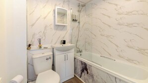 Un baño con pared de mármol, un lavabo blanco, un inodoro y una zona de ducha con mampara de vidrio.