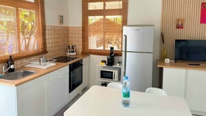 Une cuisine compacte équipée d’un réfrigérateur, d’un four à micro-ondes et d’une cuisinière. On y trouve une table à manger sur laquelle est posée une bouteille d’eau.