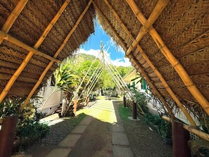 A thatched-roof structure with a central walkway surrounded by greenery.