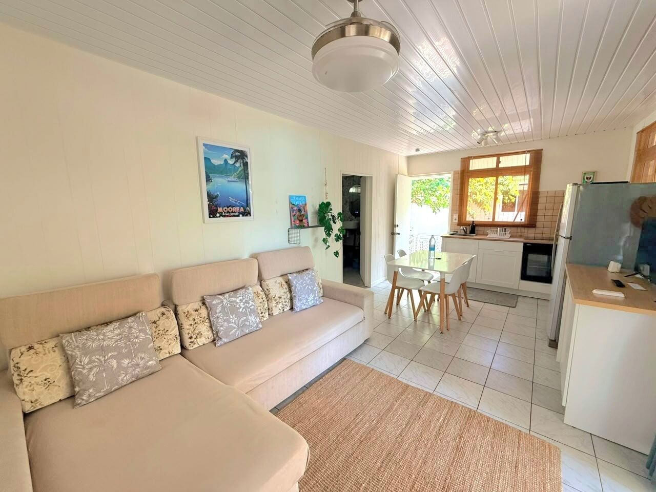 Ein Wohnzimmer mit Sofa, eine Essecke mit Tisch und Stühlen sowie eine Küche mit Kühlschrank und Herd.