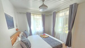 Une chambre à coucher avec un lit, des rideaux, un ventilateur de plafond et une fenêtre.